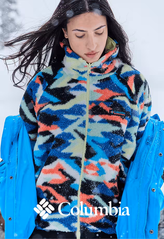 Woman wearing a colorful Columbia fleece jacket with geometric pattern, layered under a blue winter coat in snowy outdoor conditions, showcasing insulated cold-weather apparel.